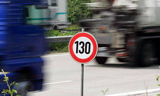 Ein Autobahnschild zur 130-km/h-Beschränkung im Vordergrund, vorbeifahrende Fahrzeuge im Hintergrund