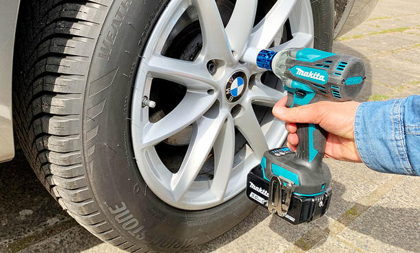 Nahaufnahme eines Rads am Auto. Eine Hand hält einen Akku-Schlagschrauber an die Radschraube.